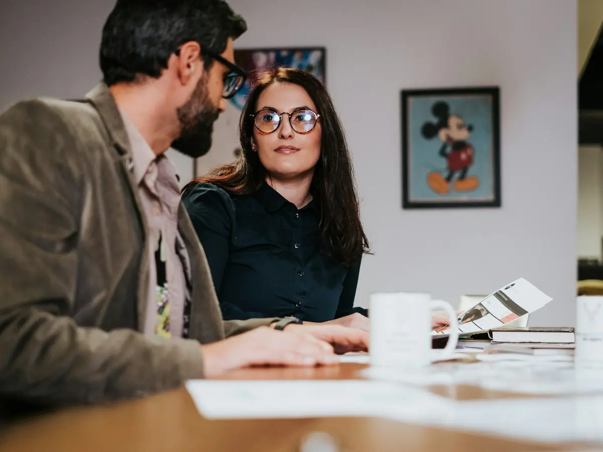 Two colleagues discussing work at a table with a laptop
